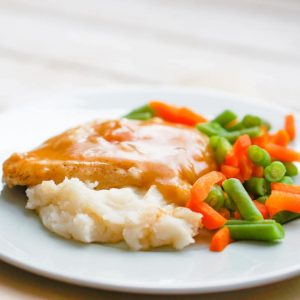 Oven baked chicken in gravy with mashed potatoes and vegetables